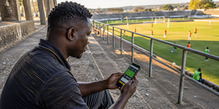 Man checks a football betting app on his smartphone from the stadium stands